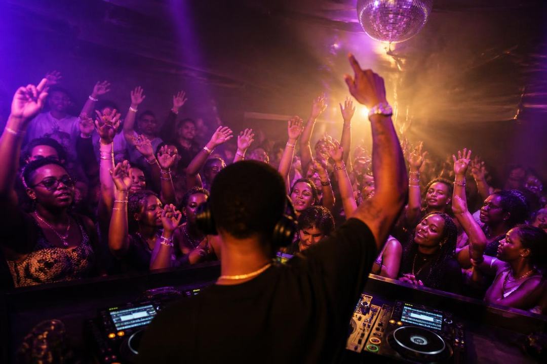A DJ facing a packed dance floor with hands in the air under purple lights